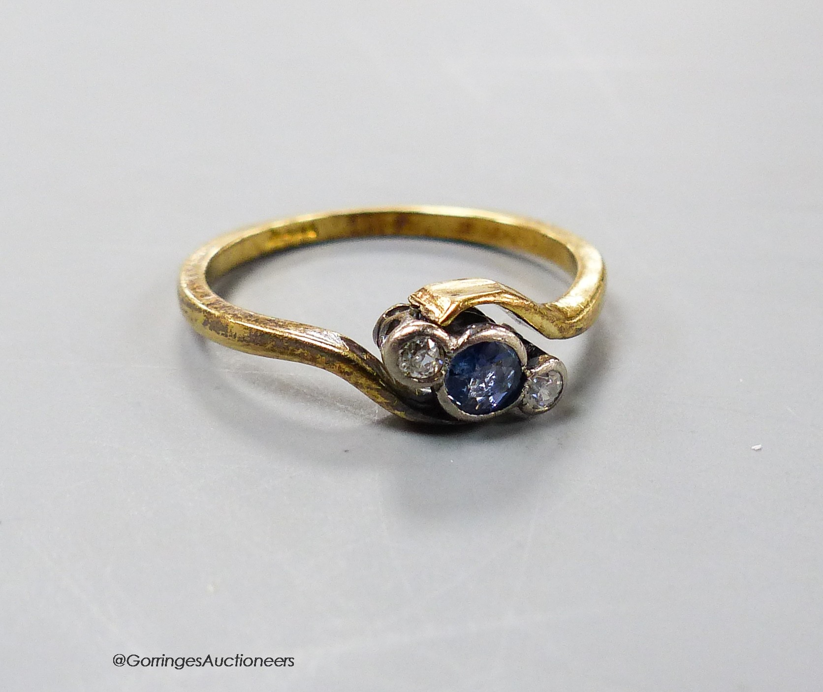 An early 20th century yellow metal, sapphire and diamond set three stone crossover ring, size L, gross 2.1 grams.